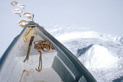 prow of boat on frozen lake with ice hole and snowshoes